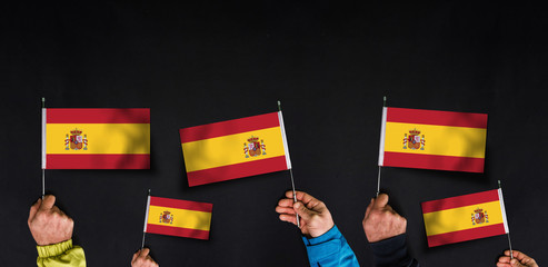 Fototapeta na wymiar Hands holds flags of Spain on dark background