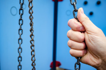 Male hand holds the forged chain from the swing, in the playground.