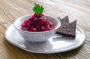 a small bowl of beetroot, walnuts, and garlic salad dressed with mayo, decorated with parsley, and served with rye bread croutons on a plate