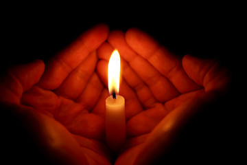 Two hands around a burning candle