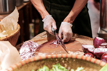 The chef in black apron cuts an onion with a knife.
