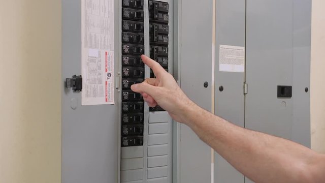 Male electrician turning off power for electrical outlet at circuit breaker box. Residential electricity power panel.
