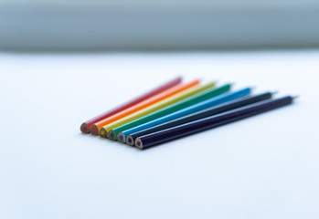 Set of seven sharp rainbow-colored pencils on a white background. Selective focus. Concept of creativity. Art supplies. Minimalism. Childhood.