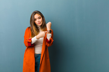 young  pretty woman looking impatient and angry, pointing at watch, asking for punctuality, wants...