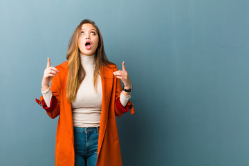 young  pretty woman feeling awed and open mouthed pointing upwards with a shocked and surprised look