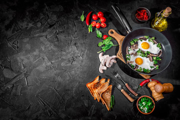Delicious breakfast or snack: scrambled eggs, bacon, mushrooms, green onions, toast and tomatoes on dark background. Top view with copy space