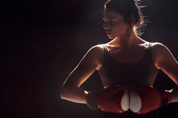 Boxing. Woman boxer in gloves standing on dark ring hands together looking aside careful