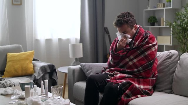 The sick man blows his nose in a napkin in the living room