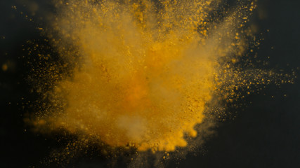 Explosion of yellow powdered paint on black background