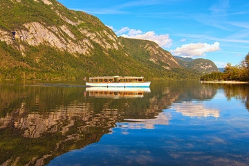 Fototapeta premium Old touristic boat on Bohinj Lake. Panoramic view of Bohinj Lake with mountain range which reflected in turquoise water. Romantic and peaceful scene. Bohinj Lake, Triglav National Park, Slovenia
