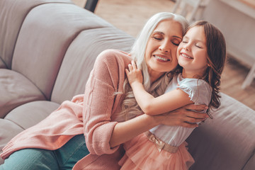 senior woman sitting on the sofa and embracing small girl with closed eyes