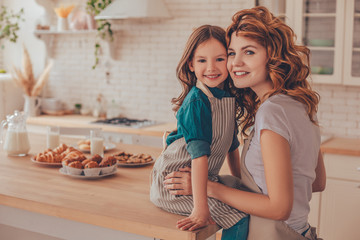 portrait of young mother and cute daughter sitting on the table and smiling at the camera on the...