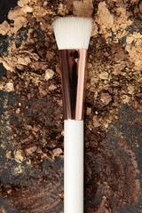 White make up brush and brown and gold eyeshadows arranged on flat stone