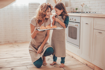 smiling woman and girl looking at each other holding tray with croissants on the kitchen