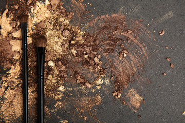 Black make up brushes and brown and gold eyeshadows arranged on flat stone