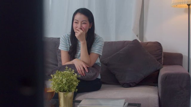 Asian middle-aged woman enjoy free time relax at home. Lifestyle girl happy fun watch drama on TV and watch entertainment in living room in modern home at night concept.