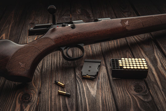 Classic bolt carbine .22lr with a wooden butt on a dark wooden surface. Weapons and cartridges for him on a wooden table.
