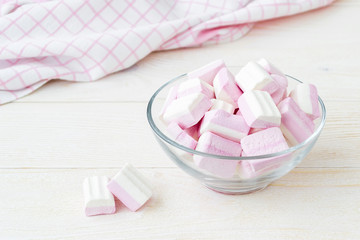 White pink fluffy marshmallows in a glass bowl on a light wooden table. Sweet and tasty winter food. Close-up delicious soft sweets.