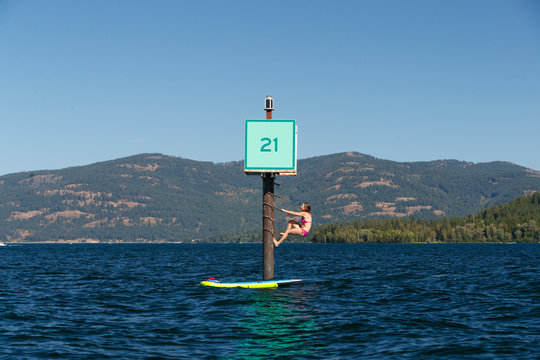 A woman in a bathing suit climbs a buey while SUPing in Lake Pend Oreille in north Idaho in summer.