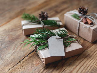 Fototapeta na wymiar Christmas presents wrapped in craft paper with natural fir tree and thuja branches as decoration. Wooden table with hand made New Year gifts.