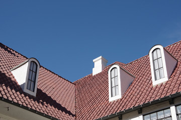 Fototapeta na wymiar Low angle view of an angled red tile roof with tall slim dormer windows under a bright blue sky
