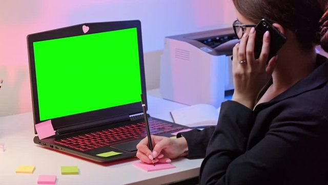 Business Woman Using Laptop Computer Pinter And Phone In Home Office. Chroma key green screen on monitor. White, pink and purple color isolated on background.