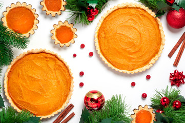 Homemade pumpkin pies and Christmas decorations on a white background, top view, flat lay. Festive winter food. Christmas baking background.