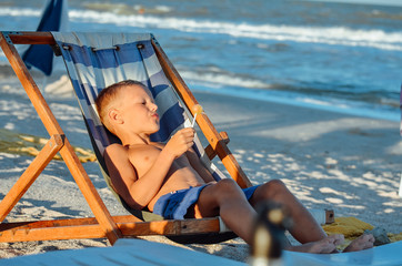 tanned baby boy resting and sunbathing in a deck chair on the sand by the blue sea