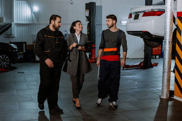 Great team in a auto service center office manager and two mechanic man have a conversation in the middle of the garage they analyzing something