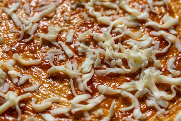 Pizza sprinkled with grated cheese before loading into the oven.