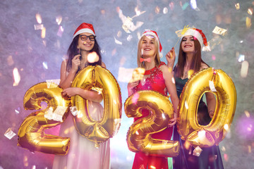 Happy and smiling women in elegant dresses posing with golden air balloons. Glossy balloons 2020, new year celebration