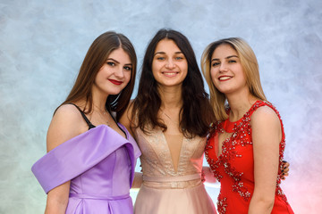 Three happy girls in elegant dresses posing on abstract background. Celebration concept