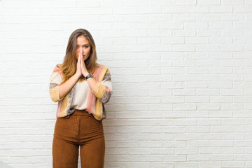 young pretty woman feeling worried, hopeful and religious, praying faithfully with palms pressed,...