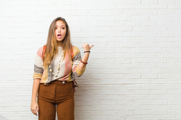 young pretty woman looking astonished in disbelief, pointing at object on the side and saying wow,...