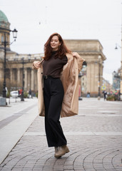 Fototapeta premium Beautiful funny naughty stylish fashionable happy girl dancing on streets of St. Petersburg city. Charming smiling woman with long dark hair, vertical