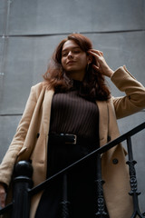 Fototapeta premium Beautiful serious stylish fashionable smart girl standing on the stairs, St. Petersburg city. Charming thoughtful woman with long dark hair, shooting from below