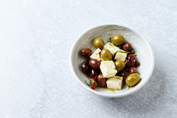 Green and kalamata olives, capers and feta cheese on bright stone background. Healthy Snack Idea. Close up. 