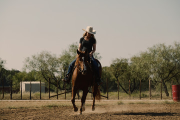 Western lifestyle shows cowgirl horseback riding quarter horse in outdoor arena 