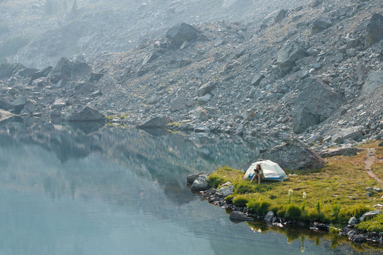 A female backpacker has her morning coffee next to Sheep Lake in the Seven Devils Mountains, Idaho, while reading from an electronic reader.
