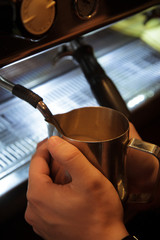 Barista men hold pitcher with milk for coffee.