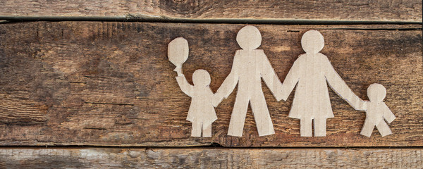 Family with two children, paper figures on wooden background
