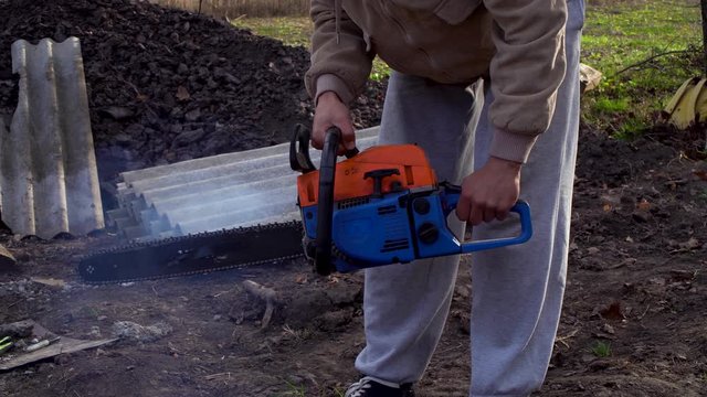 The man starts a chainsaw, a chainsaw with a two-stroke engine. The chainsaw smokes heavily