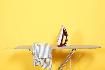 Iron and shirt on an ironing board on a colored background.