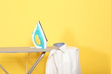 Iron and shirt on an ironing board on a colored background.