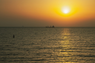 Colorful sunset in the Mediterranean sea with a cargo ship in a distance. View from the deck of a cruise ship