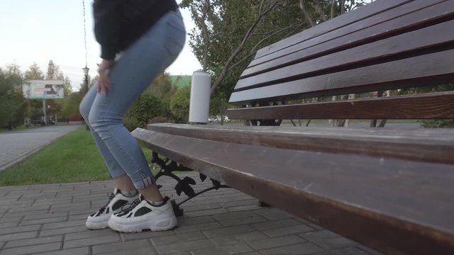 girl drinks from a metal bottle and leaves trash on a bench