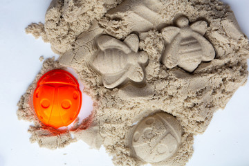 On a white background lies beige-yellow children’s kinetic sand and a plastic orange mold in the...
