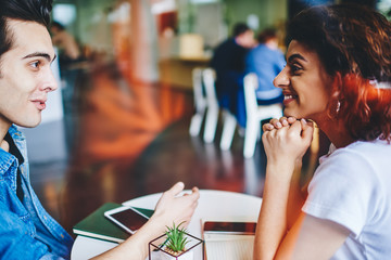Side view of happy couple in love communicating with each other and spending free time together in modern coffee shop.Positive girlfriend talking with cheerful boyfriend during meeting in cafe