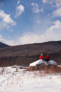Friends take a break and rest on a boulder while snowshoeing in the newly-aquired 1,300 acre parcel of land at the south end of the Green Hills Preserve. The addition expanded the overall uninterrupted acreage of the preserve to 5,500 acres and as an important watershed and drainage basin for the Saco River is an important habitat for deer, black bear, moose, bobcat, fisher, brook trout, mink, beavers and  more. Portions of the acreage are undergoing revegetation and restoration of native plant species.