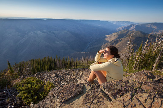A woman looks out over Hells Canyon at sunset from the Dry Diggins Lookout in the Seven Devil Mountains in central Idaho.  With a 6500+ foot slope to the Snake River at the bottom of the canyon, it is the deepest canyon in North America.